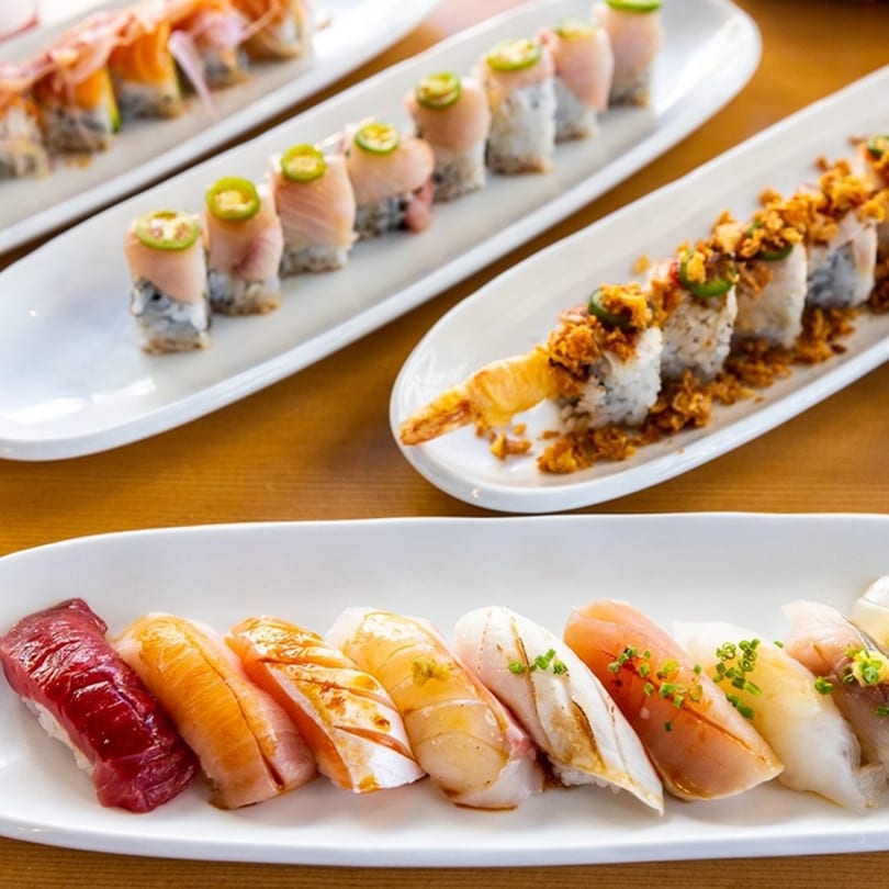 Plates of various Kombu Sushi rolls and nigiri, including spicy tuna, salmon, and shrimp tempura.