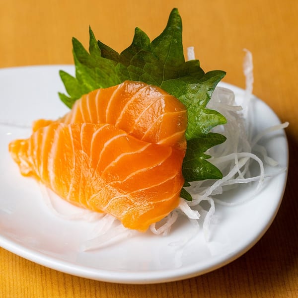 Fresh salmon sashimi slices with green shiso leaves and shredded daikon radish on a white plate.