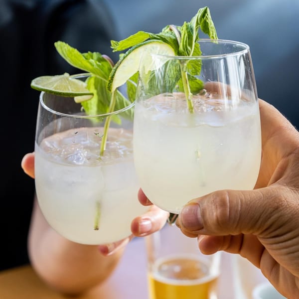 Two hands clinking glasses filled with mojito cocktails garnished with lime and mint.