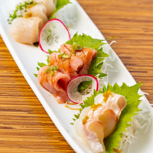 Assorted Kombu Sushi sashimi with radish, shiso leaves, and green onions on a white plate.