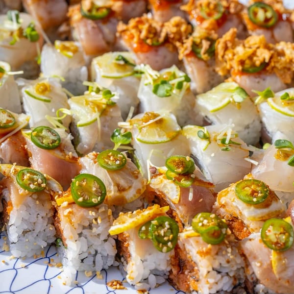 Close-up of various Kombu Sushi rolls, topped with jalapeños, lime, and crispy onions.